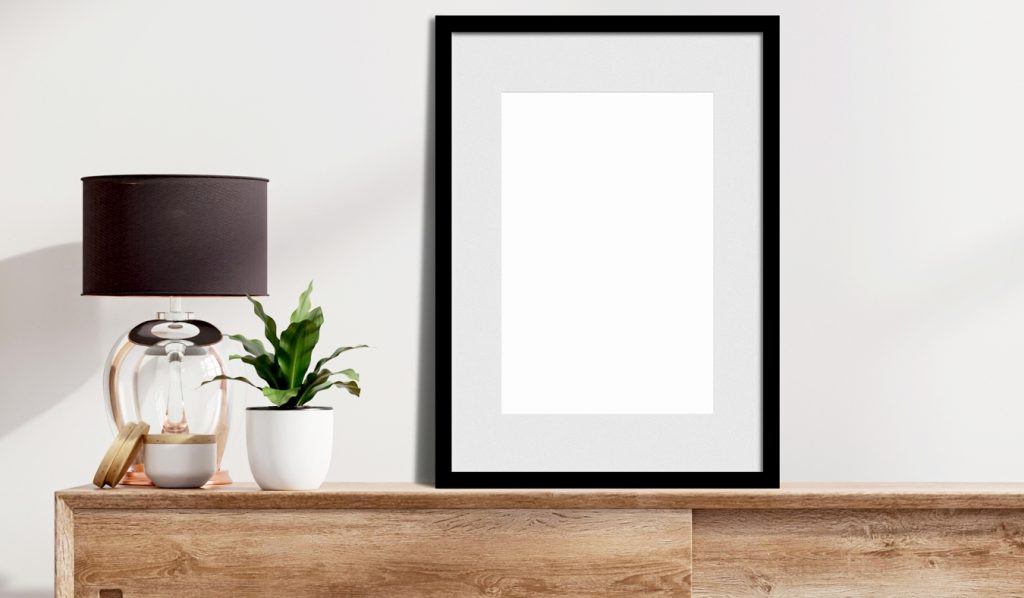 A black picture frame on a dresser by a lamp.